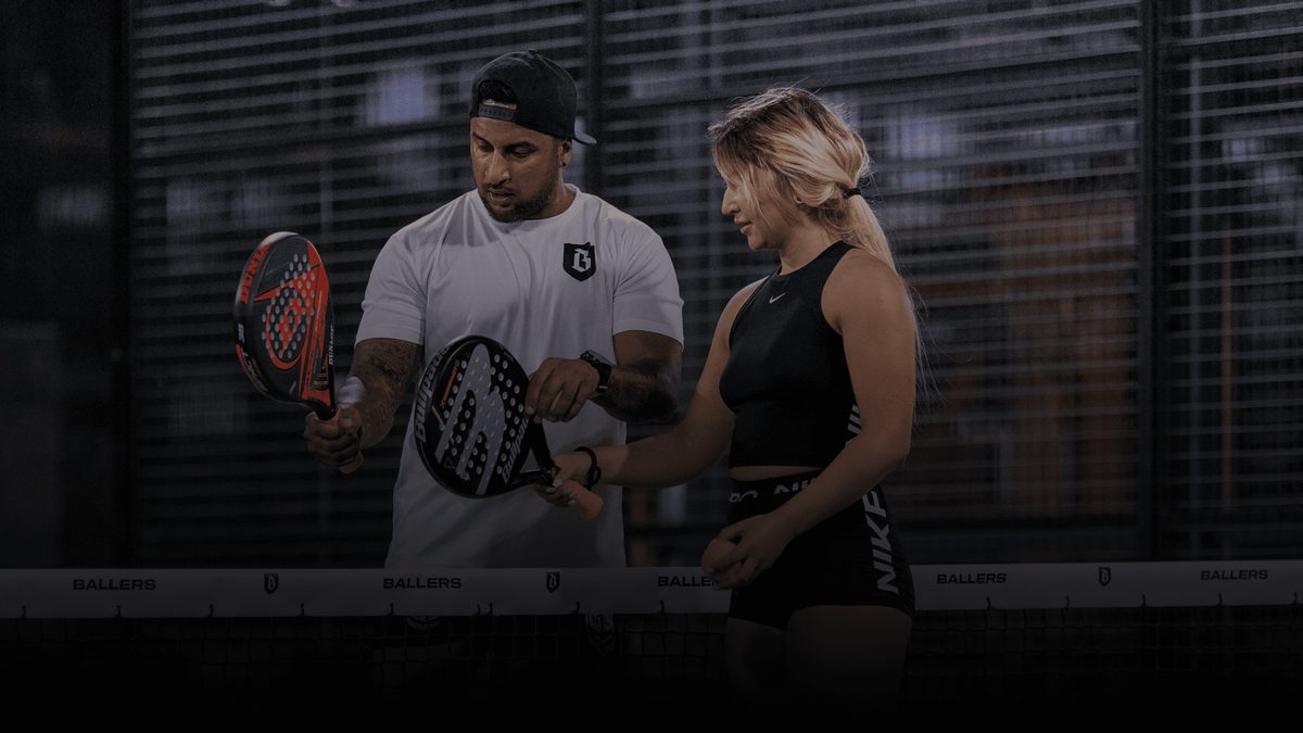 Two padel players waiting to serve, courtside under the floodlights